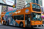 An orange double-decker sightseeing tour bus is navigating through an urban street, prominently advertising 