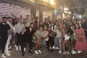 A large group of smiling people posing for a photo on a lively urban street at night.