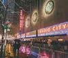 The image showcases an evening city scene with pedestrians and cars illuminated by the retro neon signage of the Music Hall