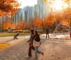 People enjoy a sunny autumn day in a park with a fountain and colorful trees with a backdrop of skyscrapers