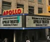 The image shows the marquee of the Apollo Theater celebrating its 75th anniversary with people walking by it on the street