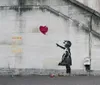 The image shows a stencil graffiti by the artist Banksy depicting a young girl reaching out toward a red heart-shaped balloon