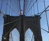 This image captures the iconic Brooklyn Bridge with its distinctive stone towers and cable arrangement in the foreground while the modern skyscrapers of Lower Manhattan including One World Trade Center create a contrasting backdrop under a clear blue sky