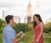 A person is proposing to their partner with a ring by a lake with city buildings in the background