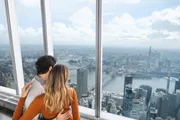 A couple is enjoying a scenic view of a cityscape from a high vantage point with large windows.