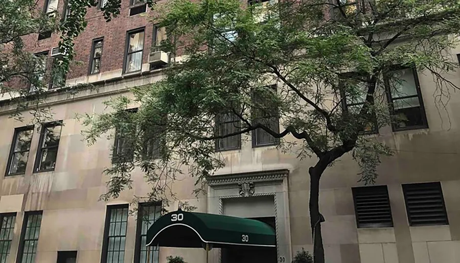 The image shows the front of an urban building with the number 30 prominently displayed above the entrance, flanked by green trees and featuring several air conditioning units in the windows.