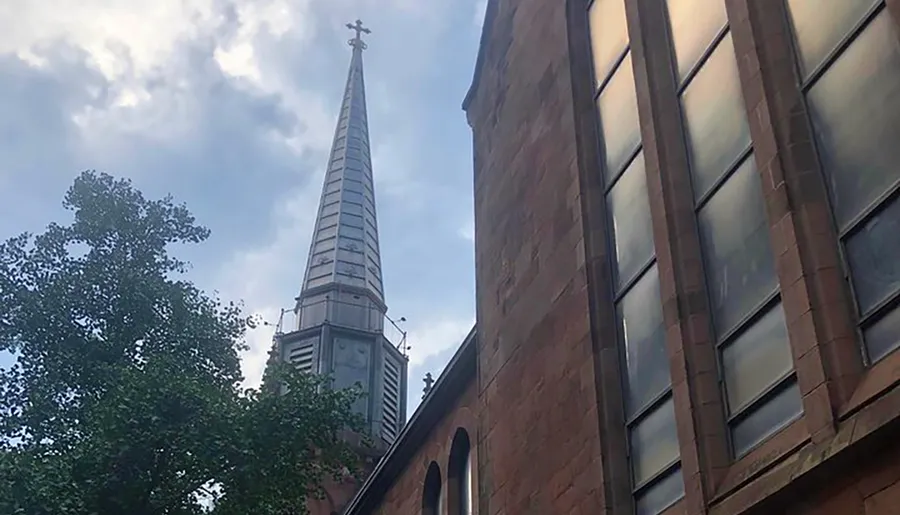 The image shows the side of a brick church with a tall steeple against a partly cloudy sky.