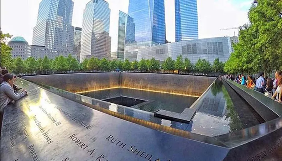 Visitors are gathered around the reflecting pool at the 9/11 Memorial in New York City, which commemorates the victims of the September 11 attacks with names inscribed around the perimeter.