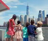 A group of children and an adult are enjoying a scenic view of the Manhattan skyline from a boat or waterfront