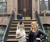 Two individuals are engaging in a pleasant conversation on the steps of a classic brownstone building