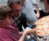 A group of people is focused on measuring a large pizza using a digital caliper
