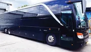 The image shows a large black bus with reflective windows parked at a depot, displaying an optical illusion that blends the side of the bus with the scenery reflected in its windows.