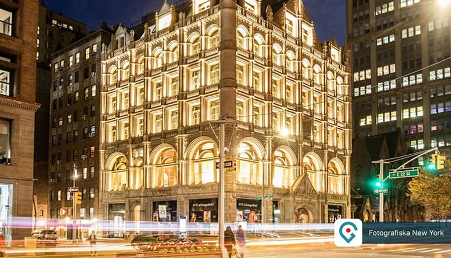 The image shows a beautifully illuminated ornate building at night with light trails from moving vehicles in the foreground, located on a street corner with a street sign for East 22nd St.