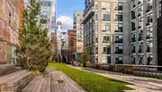 A modern urban park with wooden benches and walkways is nestled between contemporary apartment buildings on a sunny day.