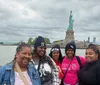 A group of people is posing for a photo with the Statue of Liberty in the background suggesting they are tourists enjoying a visit to an iconic landmark