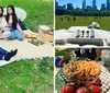 A family enjoys an outdoor picnic on a blanket with food and drinks while smiling and posing for a photo in a grassy park area