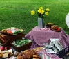 A family enjoys an outdoor picnic on a blanket with food and drinks while smiling and posing for a photo in a grassy park area