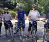 Two people with helmets are smiling for a selfie with a park featuring trees and people in the background suggesting they might be enjoying an outdoor activity like cycling