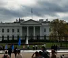 Two people are standing in front of the United States Capitol building which appears to be partially under scaffolding