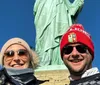 Two people are smiling for a selfie with the Statue of Liberty in the background