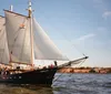 A tall ship named Clipper City with hoisted sails is filled with passengers and is sailing on the water under a clear sky