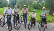 Five individuals, spanning multiple generations, are posing with their bicycles in a park, ready for a family bike ride.