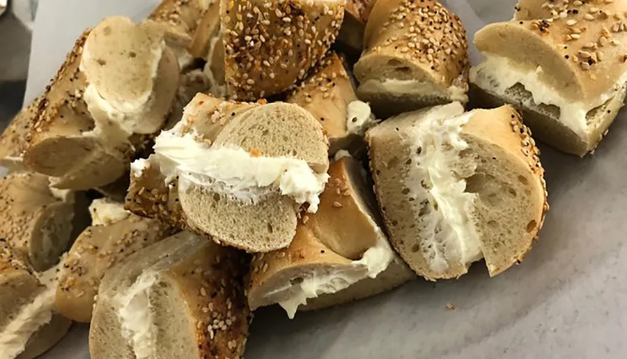 The image shows multiple slices of bagel generously smeared with cream cheese, some sprinkled with sesame seeds.