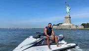 A man is sitting on a jet ski near the Statue of Liberty on a sunny day.