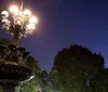 The image captures a beautifully lit angelic statue atop a fountain with water reflections in a serene park at twilight