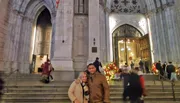 A couple is posing for a photo in front of the entrance to a cathedral adorned with Christmas decorations.