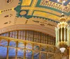 The image shows a lavishly decorated ceiling with intricate golden trimmings elaborate designs and a majestic chandelier suggesting a luxurious interior setting