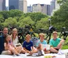 A family of six is enjoying a picnic in a park with bicycles in the background exuding a relaxed and happy atmosphere