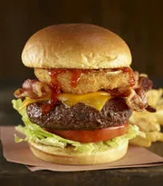 The image shows a cheeseburger with bacon, lettuce, and tomato, accompanied by fries in the background, presented on a dark backdrop.