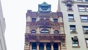 The image shows a detailed, ornate building facade next to a plainer building, typical of contrasting architectural styles in an urban environment.