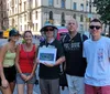 A group of people is posing for a photo on a sunny day at an urban street corner with one person holding a framed picture