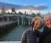 A smiling couple poses for a photo in front of a unique bridge over water at dusk