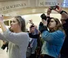 A group of people is taking photos with various cameras in a subway station near a sign that reads TICKET MACHINES SUBWAY 42ND ST