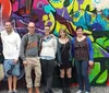 A group of smiling people is standing in front of a colorful graffiti-covered wall