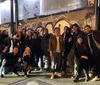 A group of smiling people is posing for a photo on a city street at night with graffiti in the background