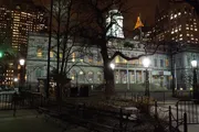 An evening view of a historic building framed by bare trees and surrounded by illuminated high-rise buildings.