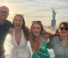 Four people are smiling and posing for a photo with the Statue of Liberty in the background likely taken from a boat or waterfront in New York