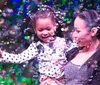 A joyful child and an adult are surrounded by a colorful swirl of bubbles sharing a moment of happiness together