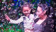 A joyful child and an adult are surrounded by a colorful swirl of bubbles, sharing a moment of happiness together.