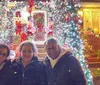 Three people pose for a photo in front of a house adorned with vibrant Christmas decorations and lights