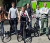 A group of five individuals is standing outdoors with bicycles on a sunny day appearing ready for a group ride