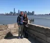 Two people are smiling for a photo with the New York City skyline in the background on a clear day