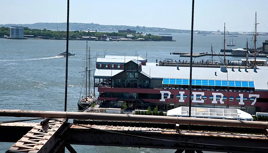 The image shows a waterfront building labeled PIER 17 with a sailing ship docked beside it, viewed from above with a body of water and land in the distance.