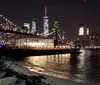 Two people are smiling for a photo in front of the Brooklyn Bridge with the Manhattan skyline in the background