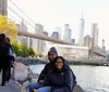 Two people are smiling for a photo in front of the Brooklyn Bridge with the Manhattan skyline in the background