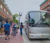 A group of tourists is gathered on a sidewalk about to board or disembarking from a tour bus on a city street